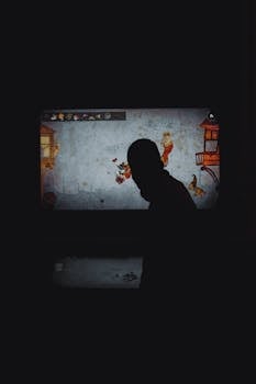 A person's silhouette in front of a colorful video game display in low light.