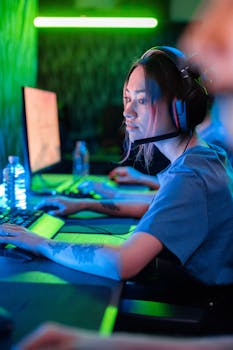 A woman deeply engaged in gaming, wearing headphones, with a visible tattoo and blue shirt.