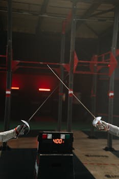 Two fencers engage in a duel with sabres. Sport timer displayed.