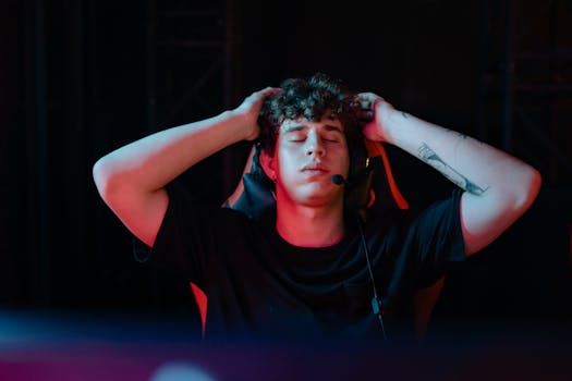 Young man with headset and tattoos, taking a break from gaming with eyes closed, seated indoors.